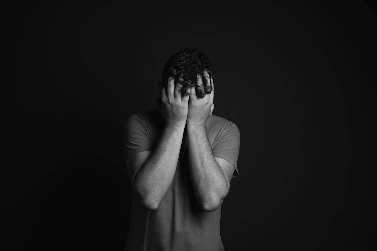 about-us A grayscale portrait of a man covering his face, depicting emotion and mental health themes.